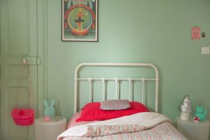 chambre d'une petite fille, mur vert d'eau avec un lit en fer forgé vintage blanc, des tables de chevet Bubu de Starck, un couvre lit fleuri dans les tons rose Petit Pan
