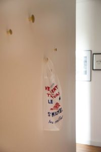 détail sur des patères en laiton The Dots de chez Muuto, un sac le Mont Saint Michel y est suspendu, le tout sur un mur blanc