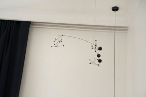 détail sur une corniche permettant de dissimuler les rails des rideaux bleu marine ainsi que les tuyaux de chauffage, il y a un mobile noir suspendu