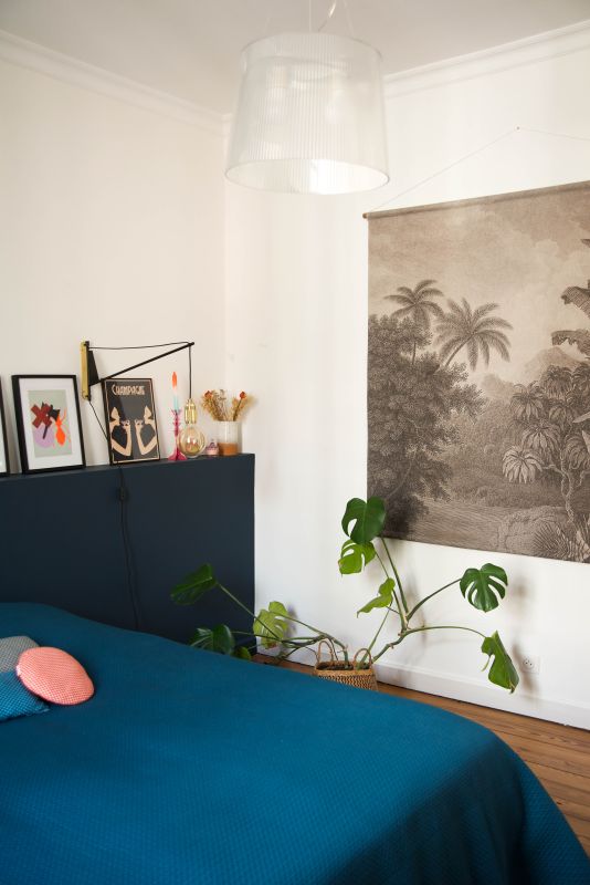 chambre avec couvre lit bleu, tenture en textile modèle Jungle de chez HK Living, tête de lit réalisé en coffrage placo et peinte en bleu marine mat de chez Farrow and ball, il y a aussi une plante, une suspension Kartell et du parquet ancien