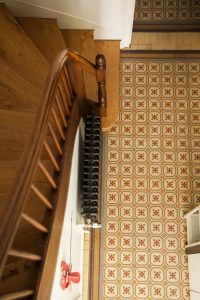 il s'agit d'une photo d'une cage d'escalier poncée et vitrifiée en orme avec vue sur les carreaux de ciment anciens de l'entrée
