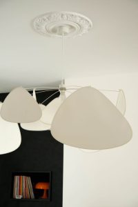 photo d'une suspension blanche Screen de chez Market Set, une moulure en plafond NMC, il y a du contraste, une niche avec des vinyles et une lampe vintage orange Nessimo de chez artemide, revêtement mural noir Facet de chez Arte