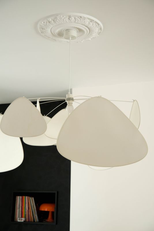photo d'une suspension blanche Screen de chez Market Set, une moulure en plafond NMC, il y a du contraste, une niche avec des vinyles et une lampe vintage orange Nessimo de chez artemide, revêtement mural noir Facet de chez Arte