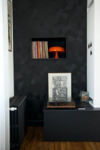 photo d'une niche avec des vinyles et une lampe vintage orange Nessimo de chez artemide, revêtement mural noir Facet de chez Arte, platine vinyles, radiateur en fonte noir et parquet ancien