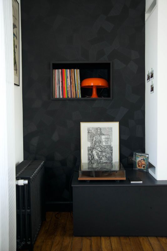photo d'une niche avec des vinyles et une lampe vintage orange Nessimo de chez artemide, revêtement mural noir Facet de chez Arte, platine vinyles, radiateur en fonte noir et parquet ancien