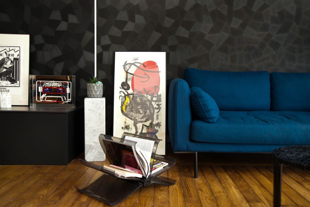 photo d'un salon avec un canapé bleu en laine bouillie, aussi, un porte revue de chez Kartell, revêtement mural noir Facet de chez Arte, du parquet ancien poncé et vitrifié, il y a aussi une sérigraphie Miro