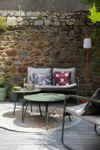 terrasse en lame de bois IPE avec salon de jardin Kaki Pantone, coussins Podevache et lampe Fermob orange, mur en pierre
