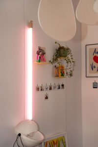 photo de détail sur pan de mur avec étagères jaunes Moustache, néon rose fluo Seletti, lampe Eclipse,