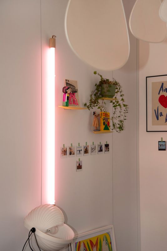 photo de détail sur pan de mur avec étagères jaunes Moustache, néon rose fluo Seletti, lampe Eclipse,