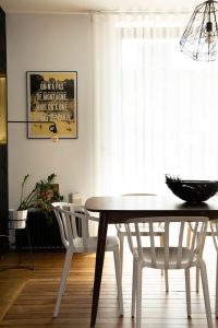 photo d'une salle à manger comprenant une table en noyer et des chaises blanches Venice de chez Kartell, parquet ancien poncé et vitrifié, voilage blanc, radiateur en fonte noir